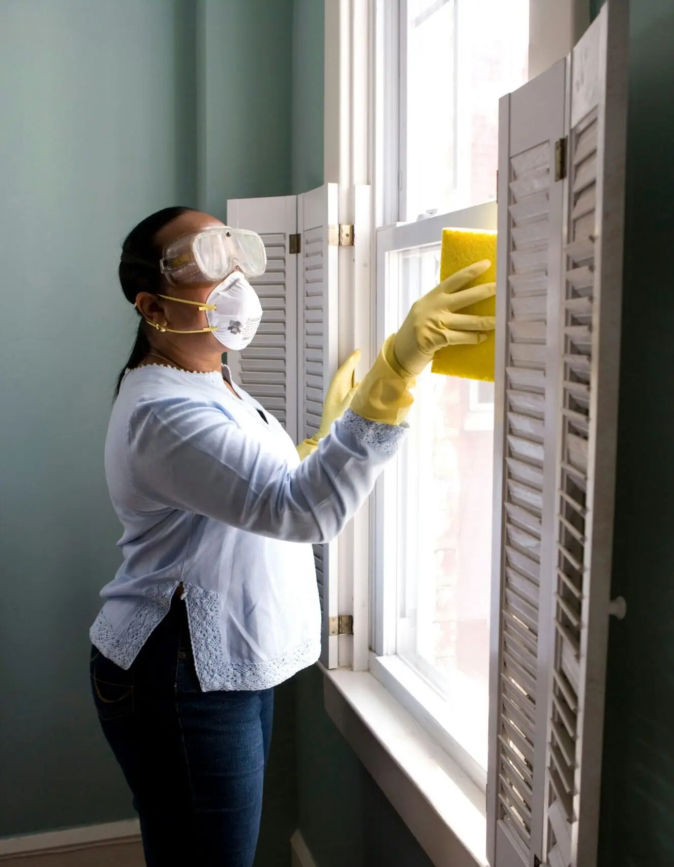 Cleaning employee washing a window with a mask and yellow gloves