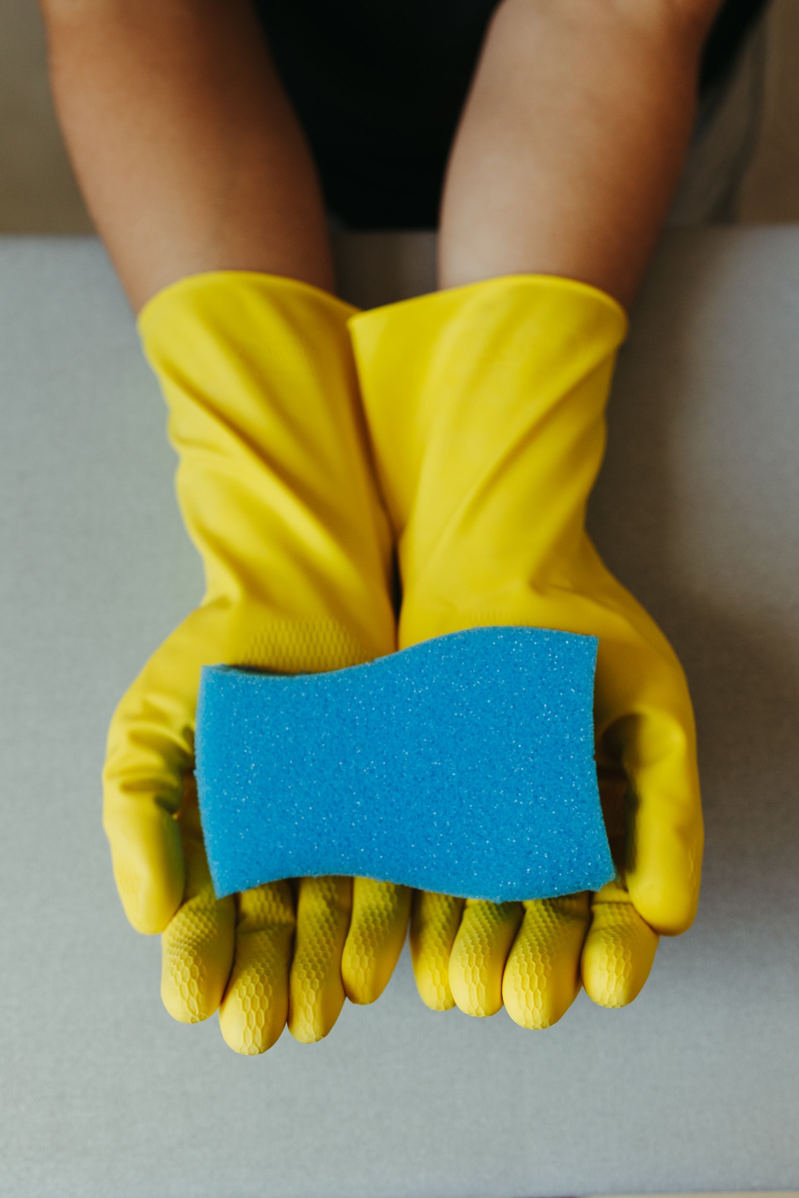 Yellow-gloved hands holding a blue sponge