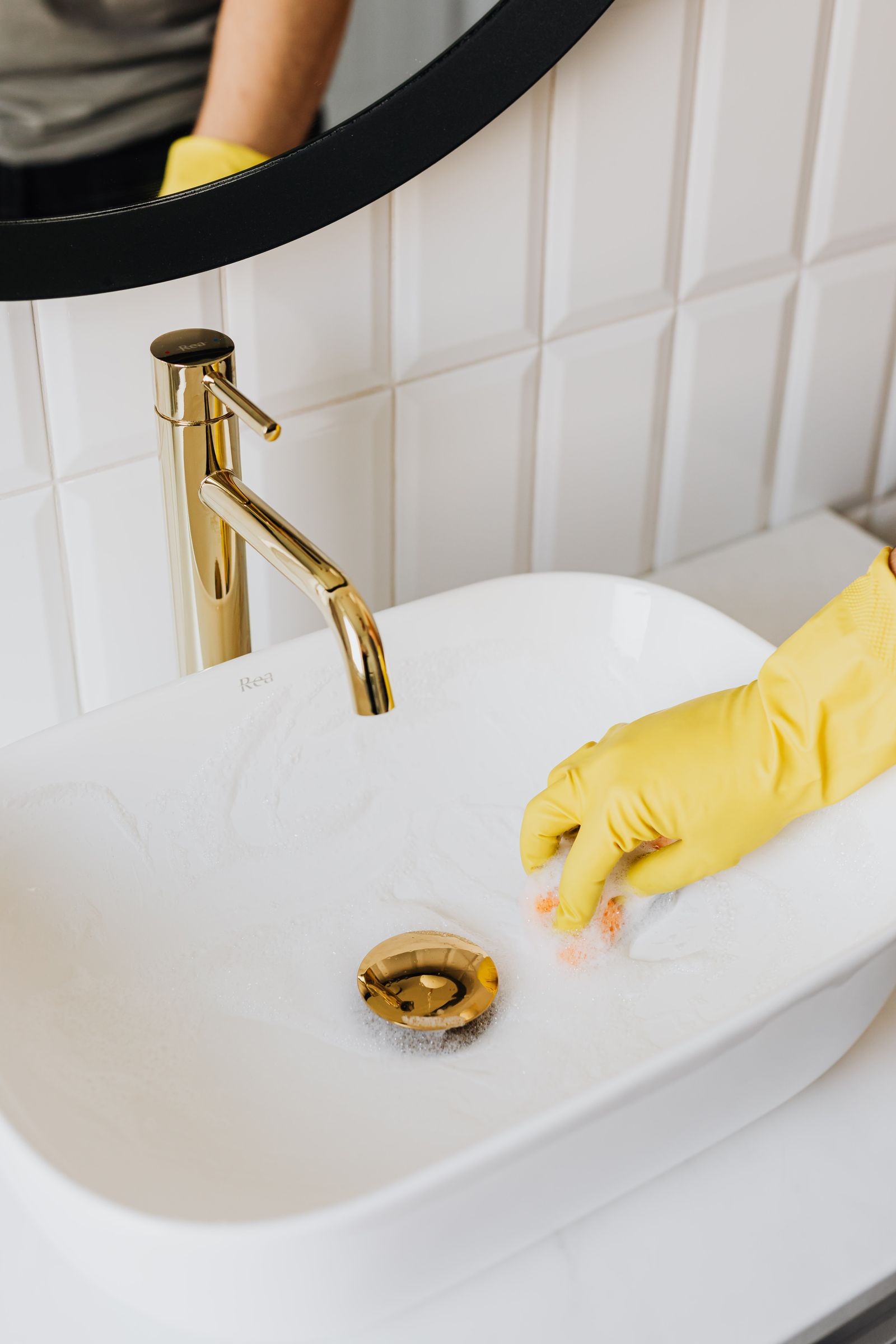 Yellow glove cleaning a sink with a gold faucet