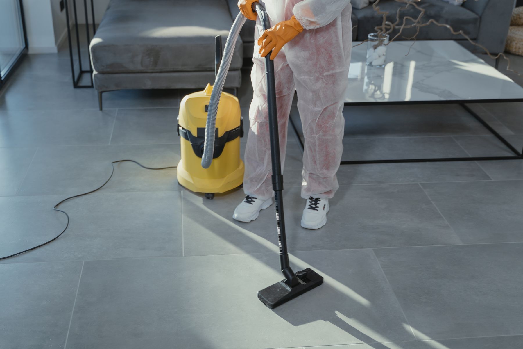 Technicien en combinaison de protection qui aspire un plancher