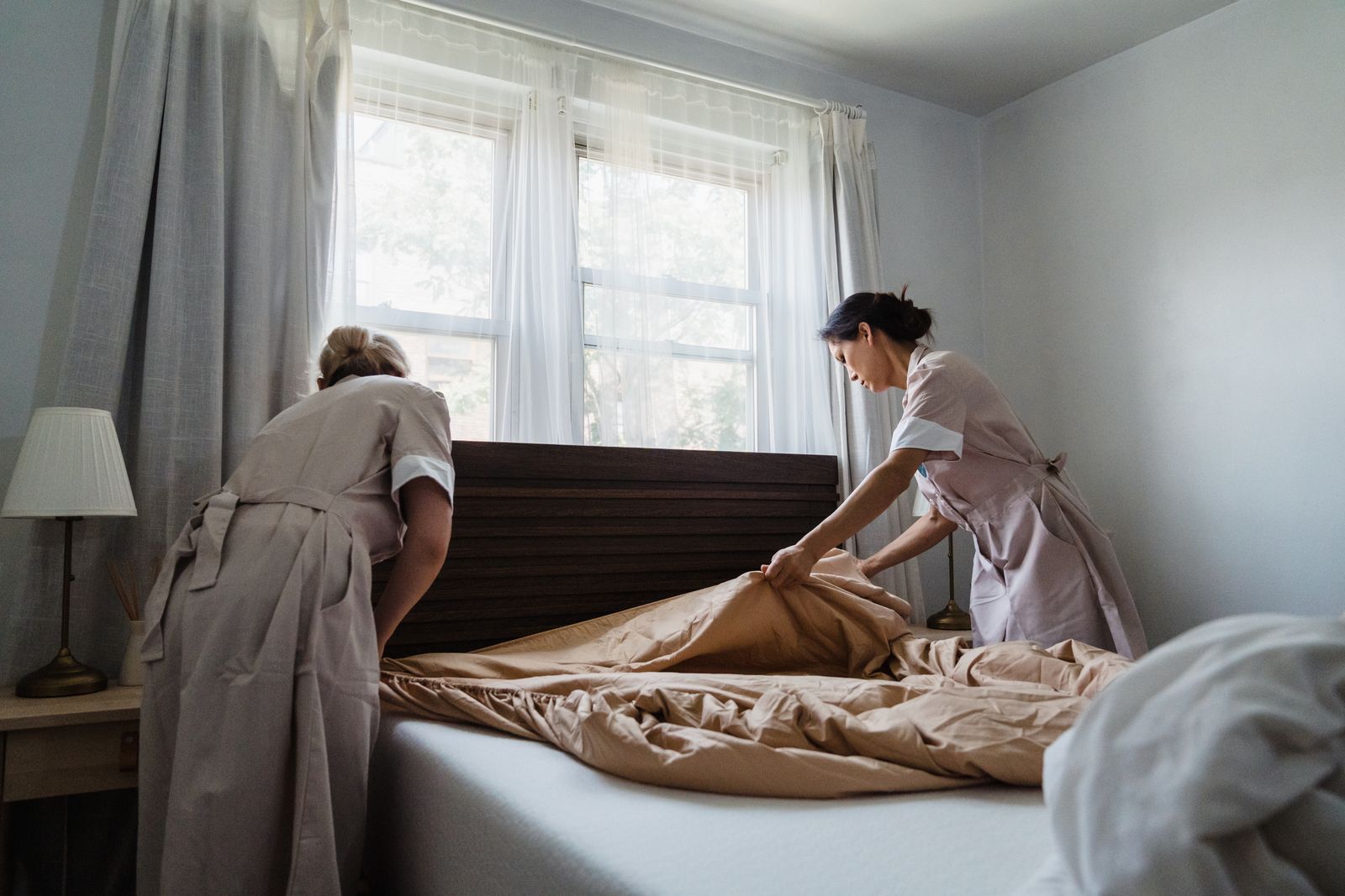 Two employees making a bed in a bright bedroom