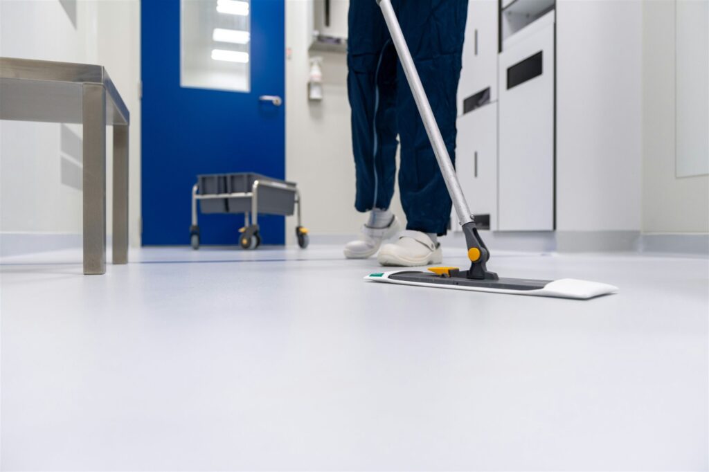 Employé qui lave un plancher blanc avec une vadrouille plate